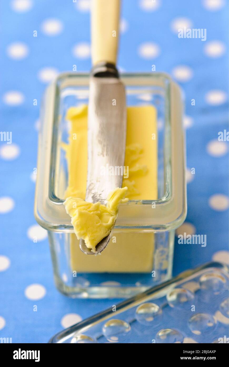 Butterdose aus Glas mit Buttermesser auf blau-weiß gepunkteten Tuch - Stockfoto