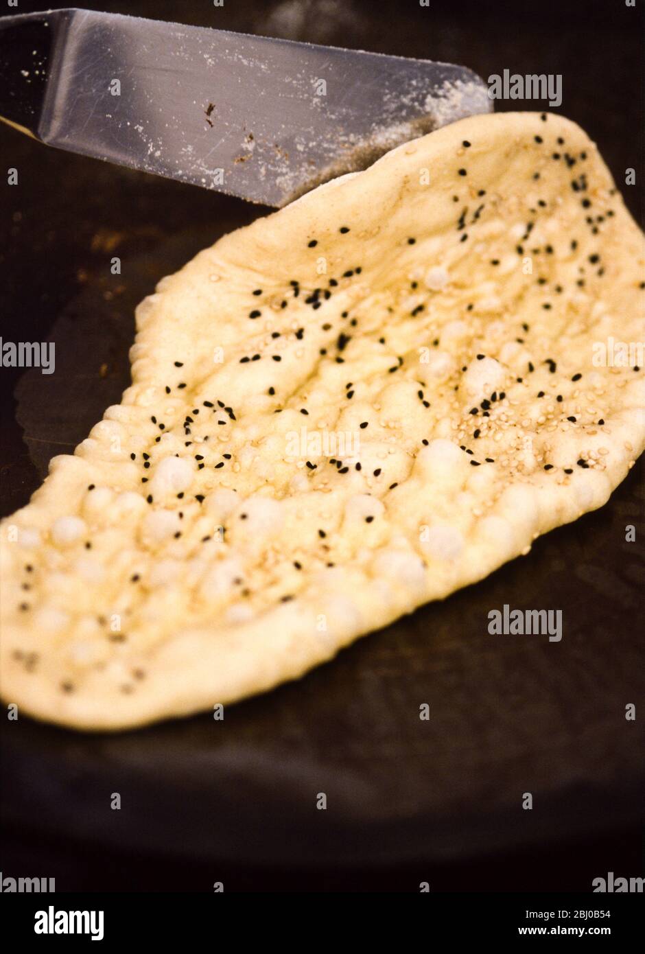 Selbstgebackenes Naan-Brot, das vom Backblech gehoben wird - Stockfoto