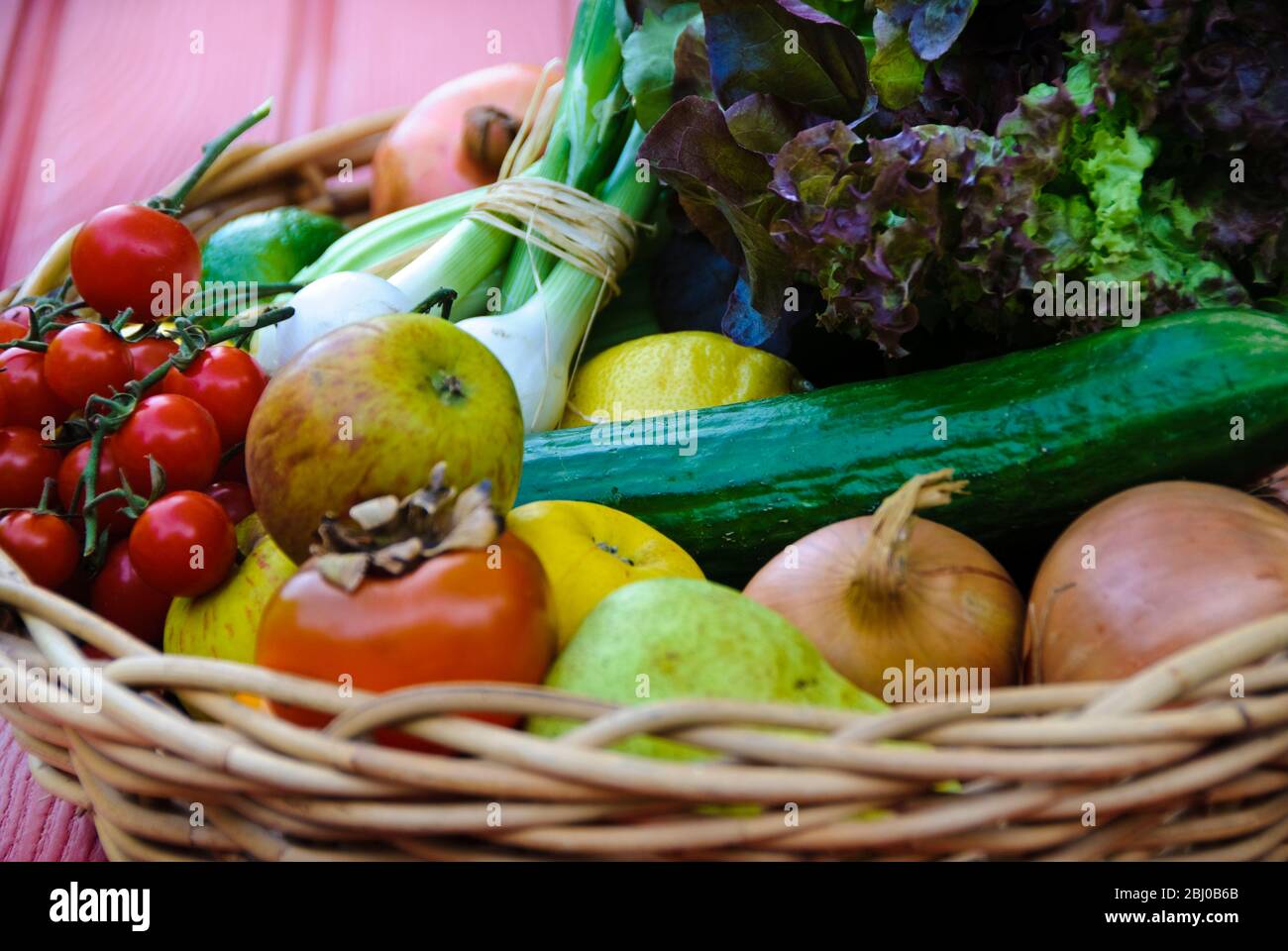 Korb mit frischem Obst und Gemüse auf roter Oberfläche - Stockfoto