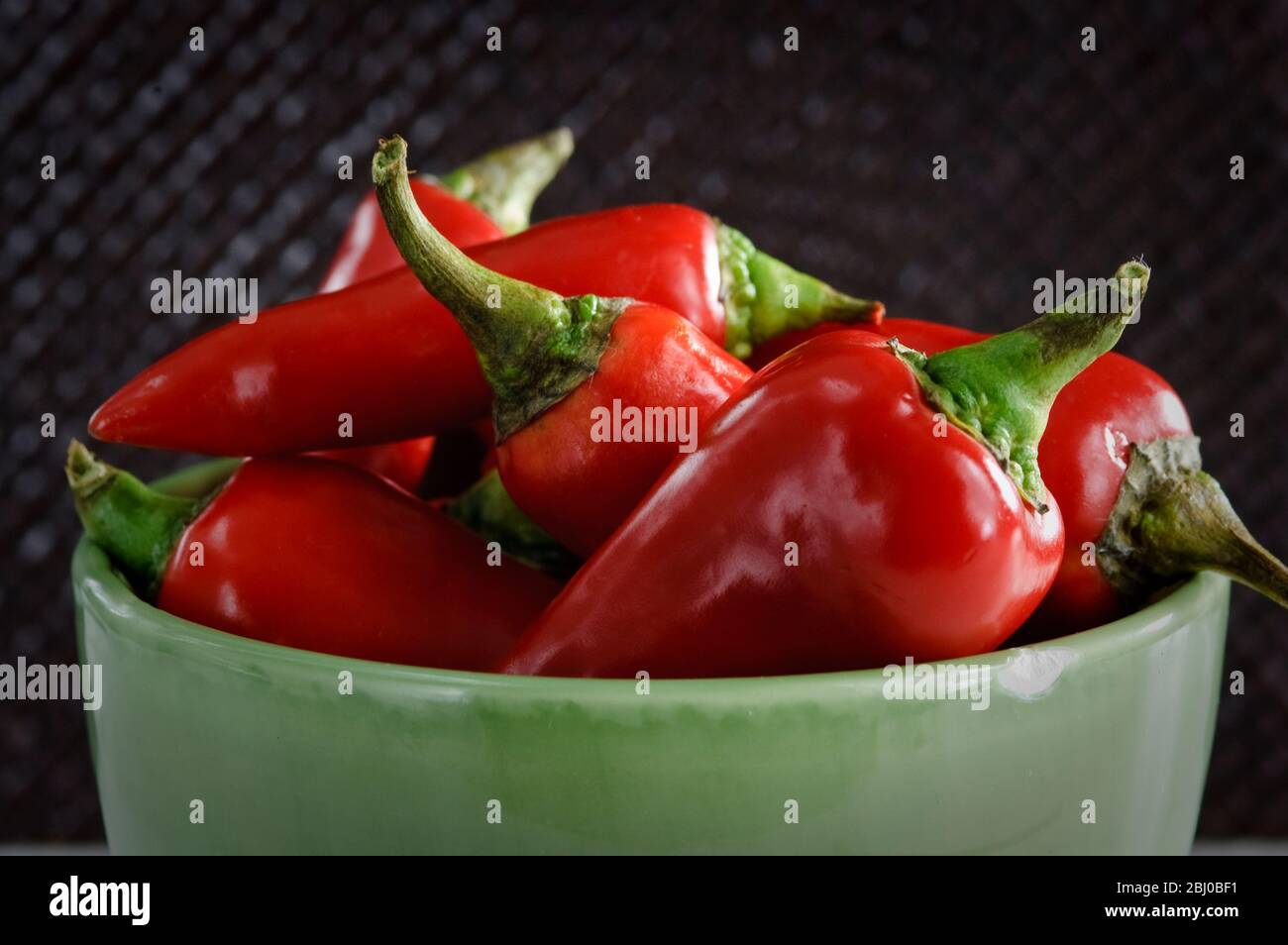 Glänzende rote Chilischoten in grüner Schüssel - Stockfoto