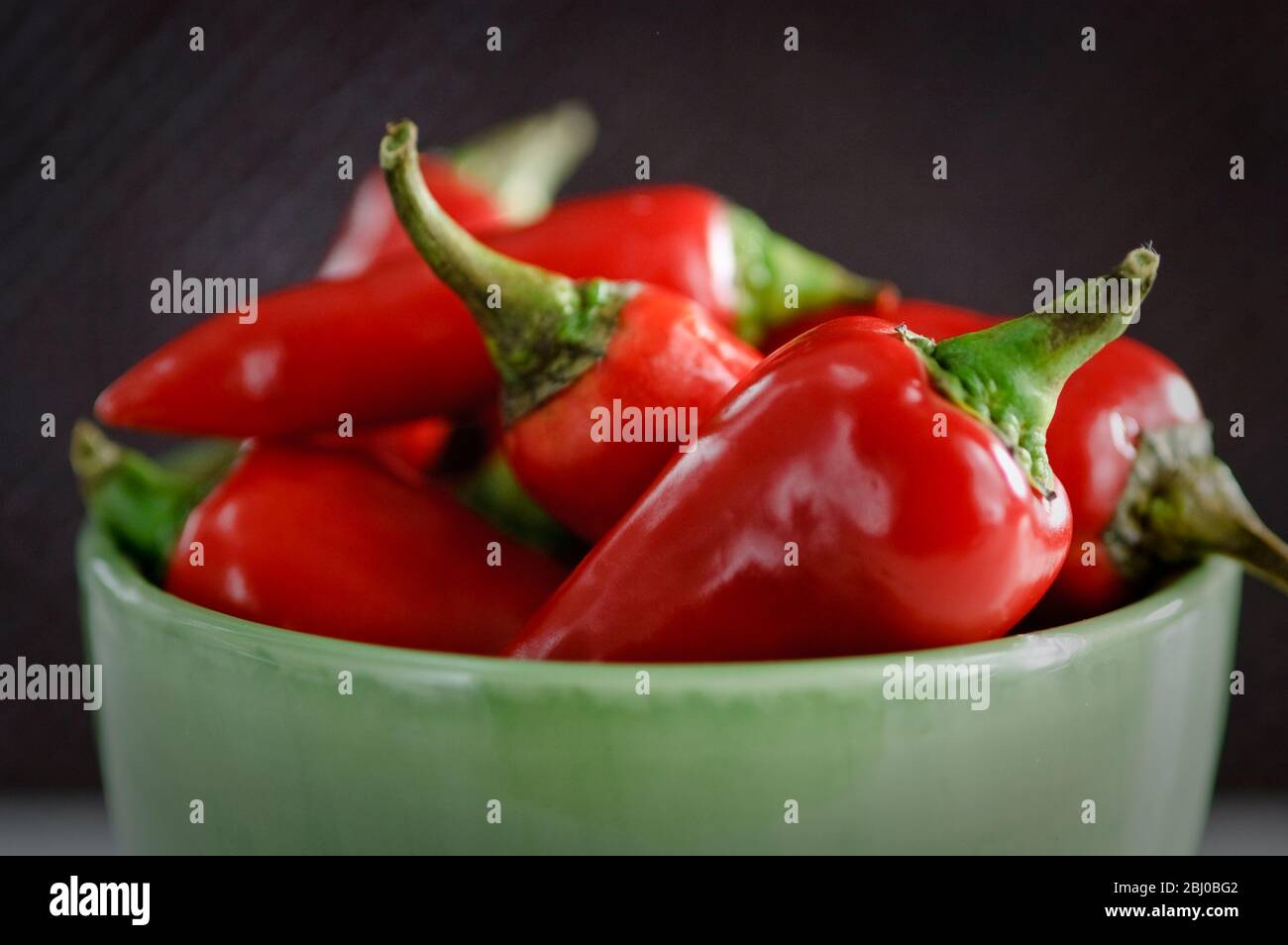 Glänzende rote Chilischoten in grüner Schüssel. Kürzere Schärfentiefe. - Stockfoto