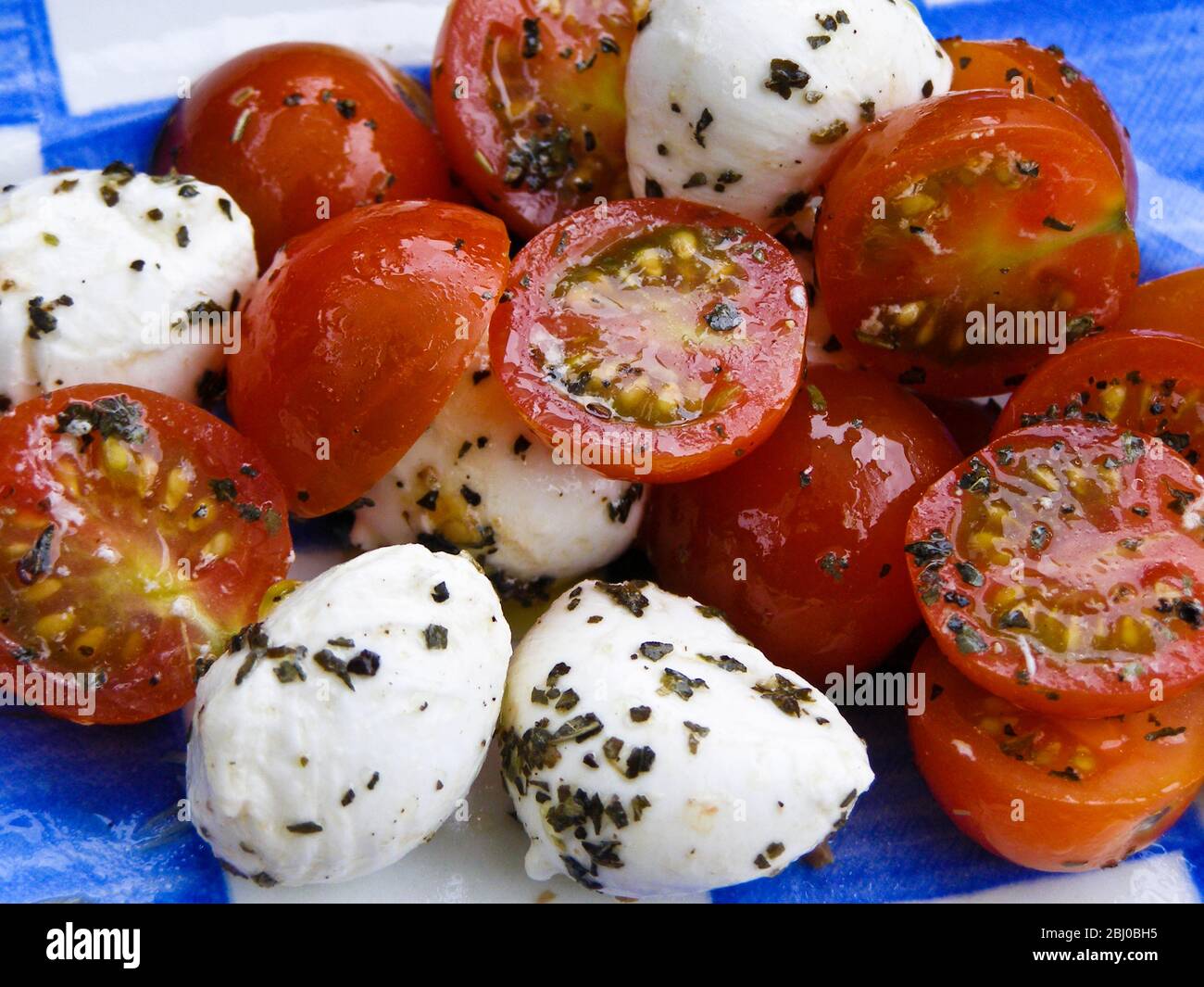 Salat aus Mozzarella-Kugeln mit Kirschtomaten in Öl, Essig und Kräuterdressing. - Stockfoto