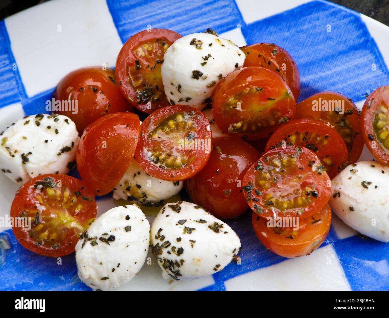 Salat aus Mozzarella-Kugeln mit Kirschtomaten in Öl, Essig und Kräuterdressing. - Stockfoto