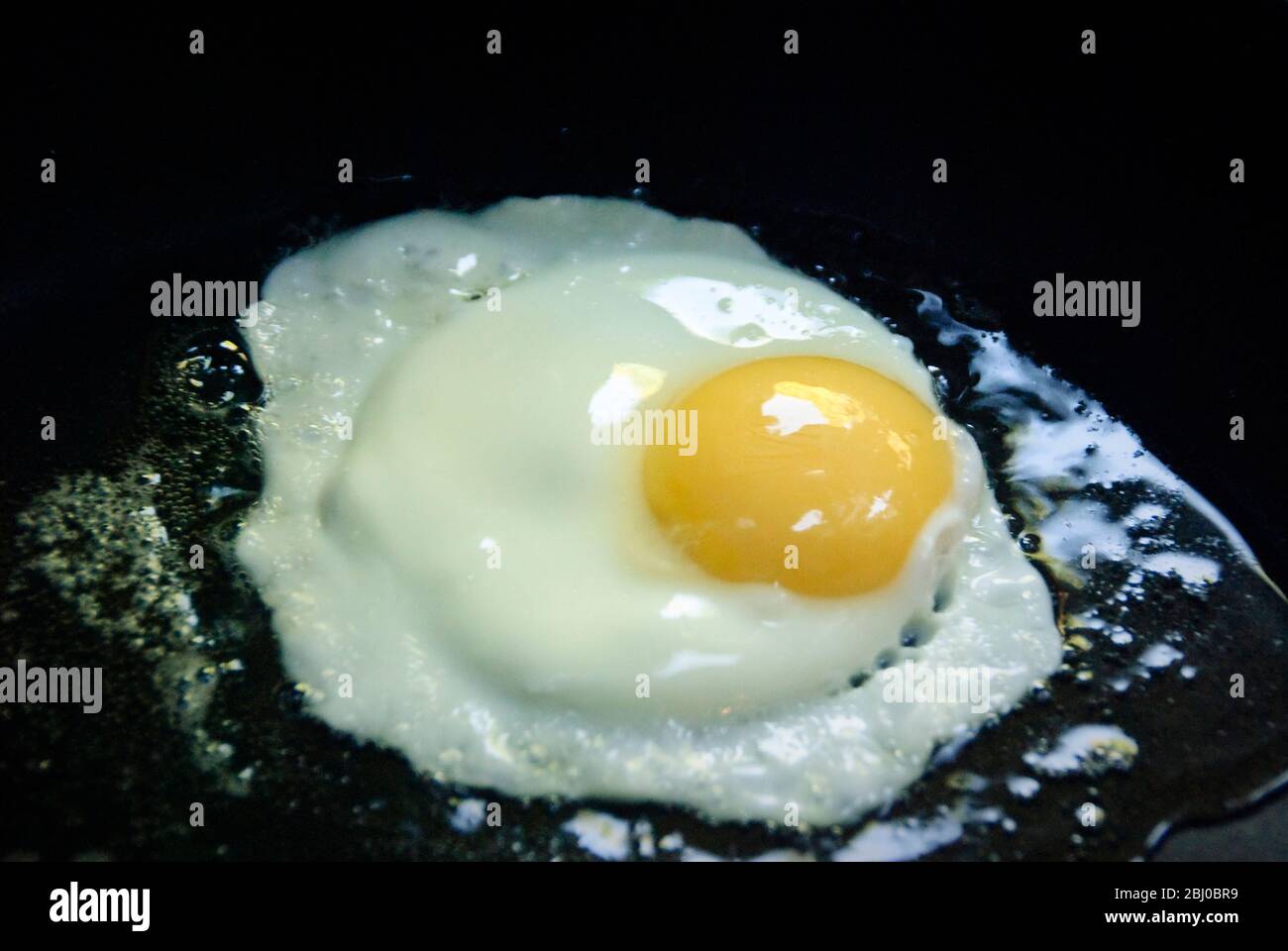Frische Bio-Eier aus Freilandhaltung werden in schwarzer Antihaftpfanne gebraten - Sonnenseite nach oben - Stockfoto