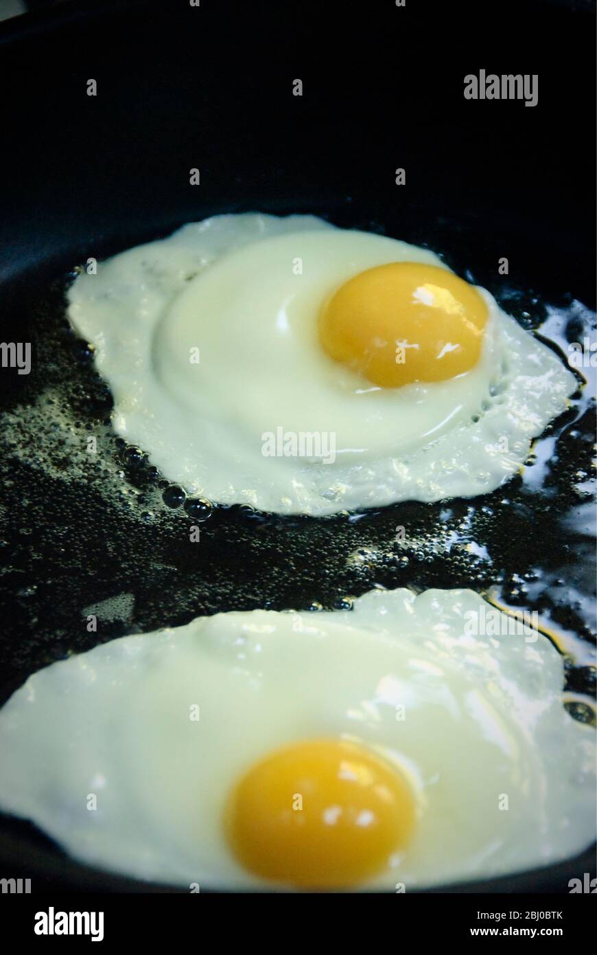 Frische Bio-Eier aus Freilandhaltung werden in schwarzer Antihaftpfanne gebraten - Sonnenseite nach oben - Stockfoto