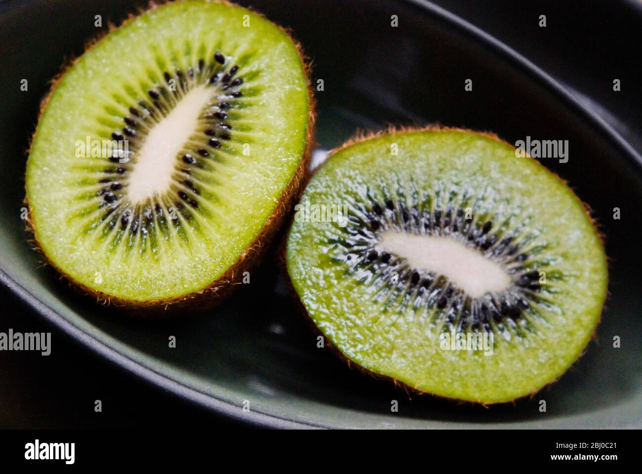 Halbierte Kiwi-Früchte auf schwarzem Teller - Stockfoto