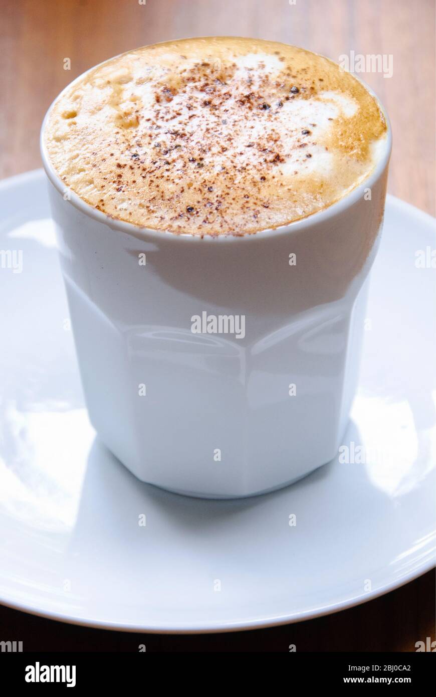 Cappuccino mit schaumigen Topflappen in einer handlosen Tasse mit abgestaubtem Kakao. - Stockfoto