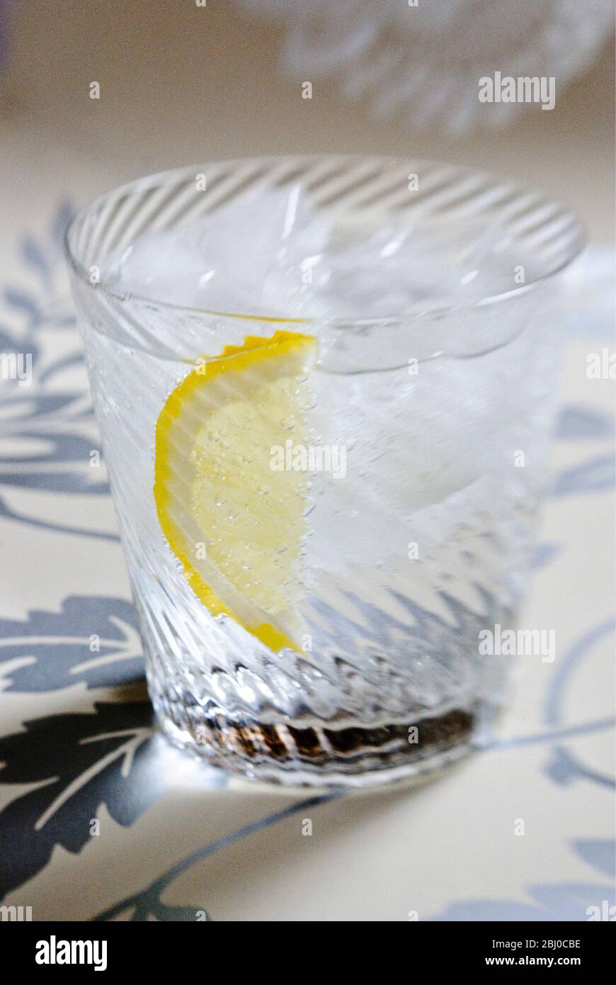 Feine Spirale geblasen Glas von klarem Geist mit Soda oder Tonic, und Scheibe Zitrone auf dekorativem Hintergrund - Stockfoto