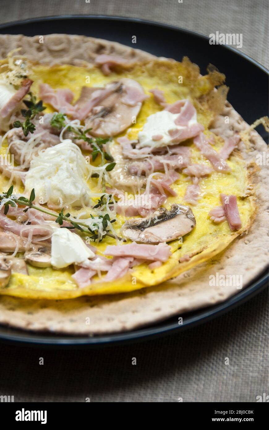 Omelette im dünnen Pfannkuchen-Stil mit Pilz, Schinken, Ziegenkäse und Parmesan auf dünnem schwedischen Brot, bevor es als tragbares Frühstück aufgerollt wird. - Stockfoto