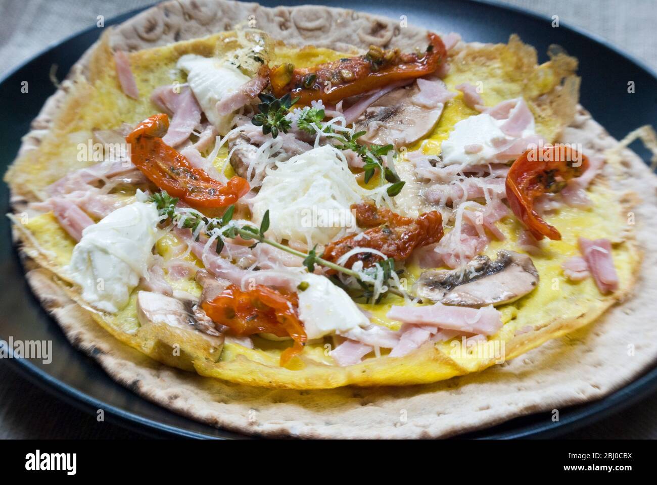 Omelette im dünnen Pfannkuchen-Stil mit Pilz, Schinken, getrockneten Tomaten, Ziegenkäse und Parmesan auf dünnem schwedischen Brot, bevor es als porta aufgerollt wird Stockfoto