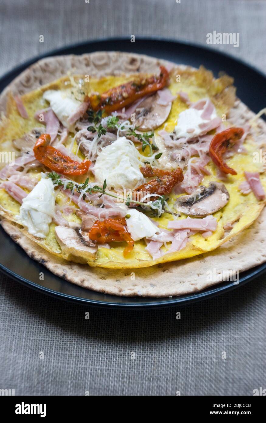 Omelette im dünnen Pfannkuchen-Stil mit Pilz, Schinken, getrockneten Tomaten, Ziegenkäse und Parmesan auf dünnem schwedischen Brot, bevor es als porta aufgerollt wird Stockfoto