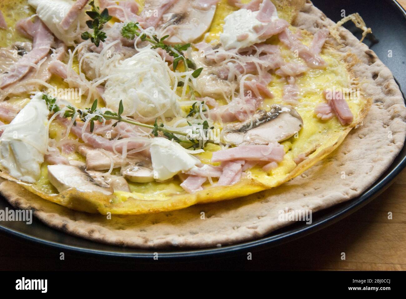 Omelette im dünnen Pfannkuchen-Stil mit Pilz, Schinken, Ziegenkäse und Parmesan auf dünnem schwedischen Brot, bevor es als tragbares Frühstück aufgerollt wird. - Stockfoto