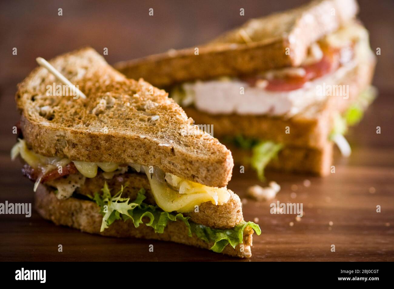Geröstetes Club-Sandwich mit Huhn, Käse, Tomaten und Salat auf braunem Brot. - Stockfoto