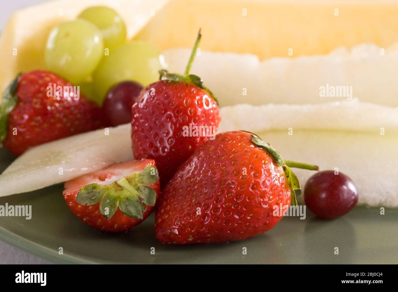 Frischer Obstsalat aus Erdbeeren, Trauben und Scheiben Melone und Ananas auf grünem Teller. - Stockfoto