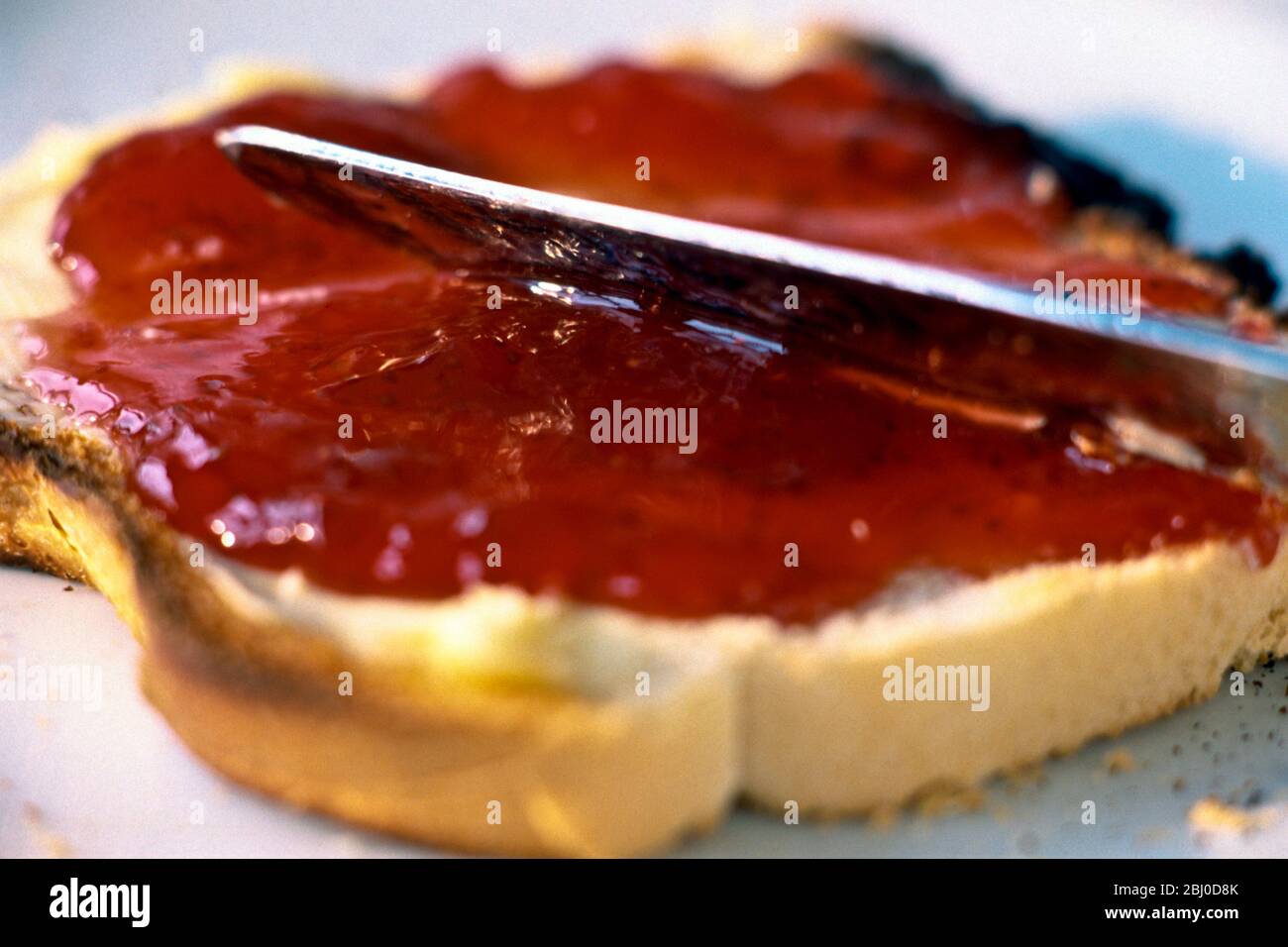 Erdbeermarmelade dick auf weißes geröstetes Brot verteilen. - Stockfoto