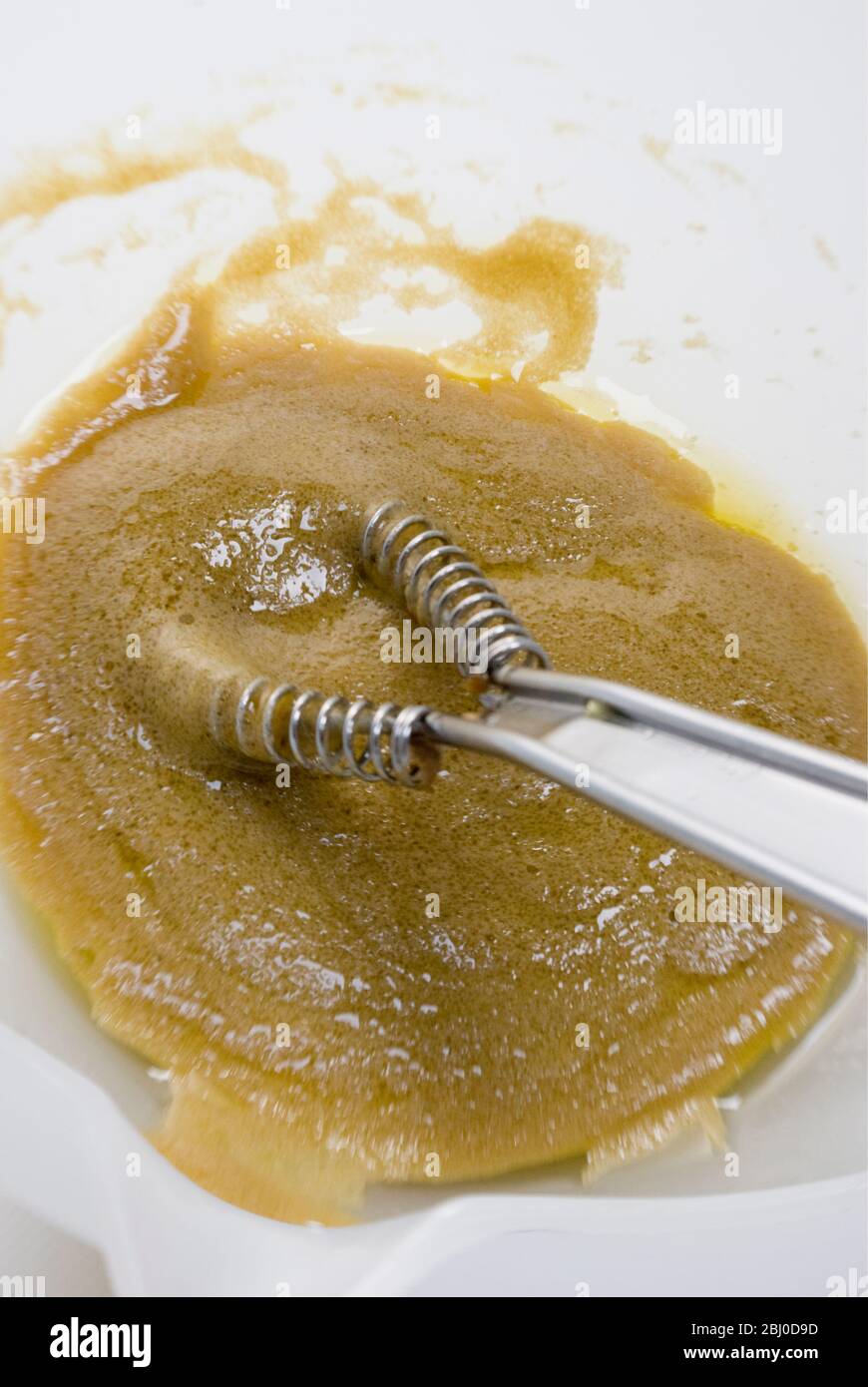 Herstellung von klassischen Französisch Vinaigrette Dressing mit Senf, Olivenöl und Rotwein Essig zusammen in weißen Schüssel geschlüpft - Stockfoto