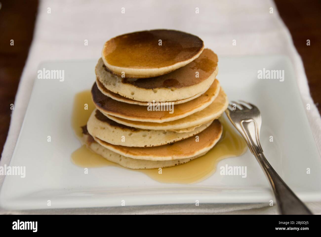 Stapel von schottischen Pfannkuchen auf weißem Teller mit silberner Gabel und Ahornsirup - Stockfoto