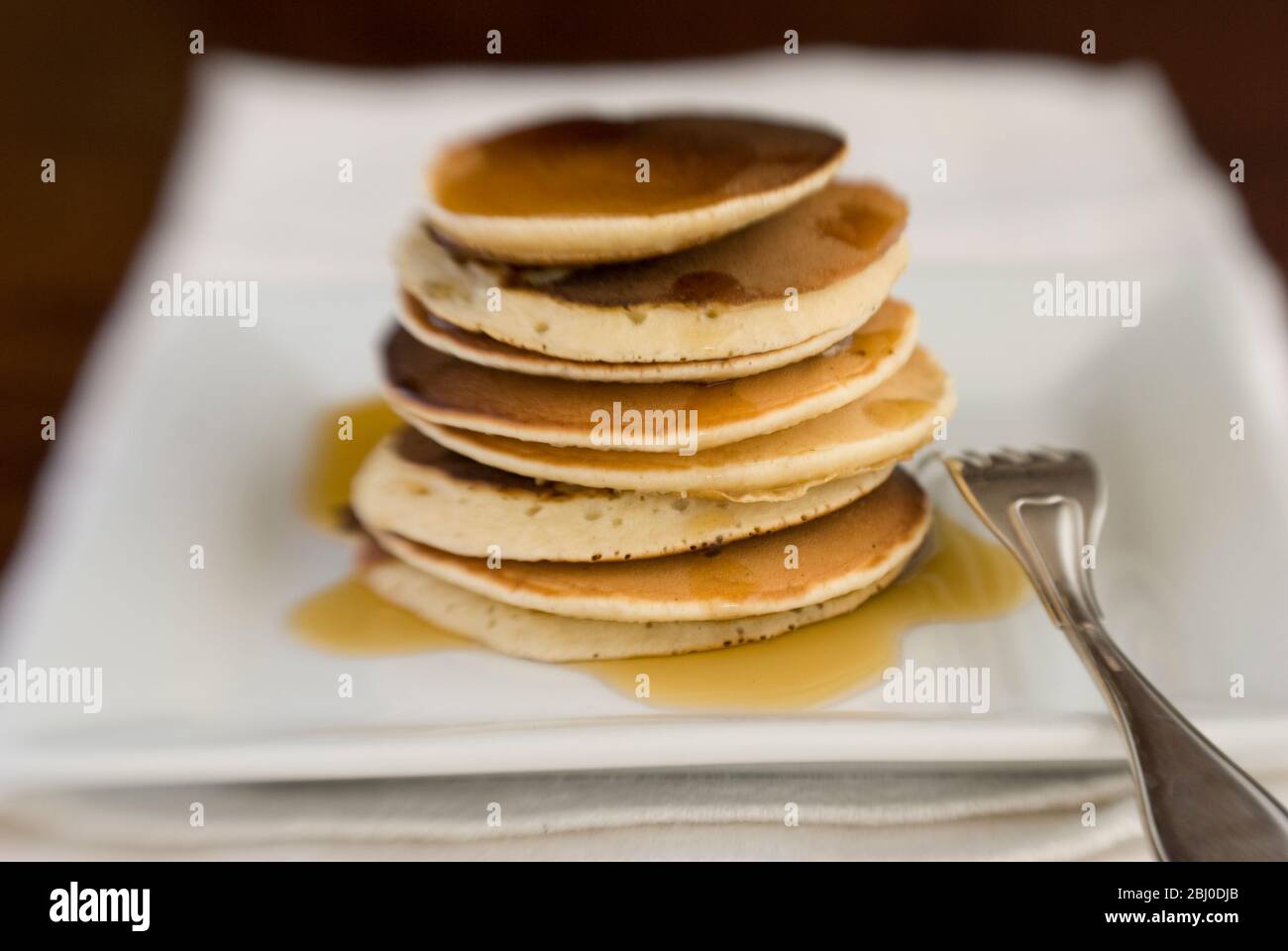 Stapel von schottischen Pfannkuchen auf weißem Teller mit silberner Gabel und Ahornsirup - Stockfoto