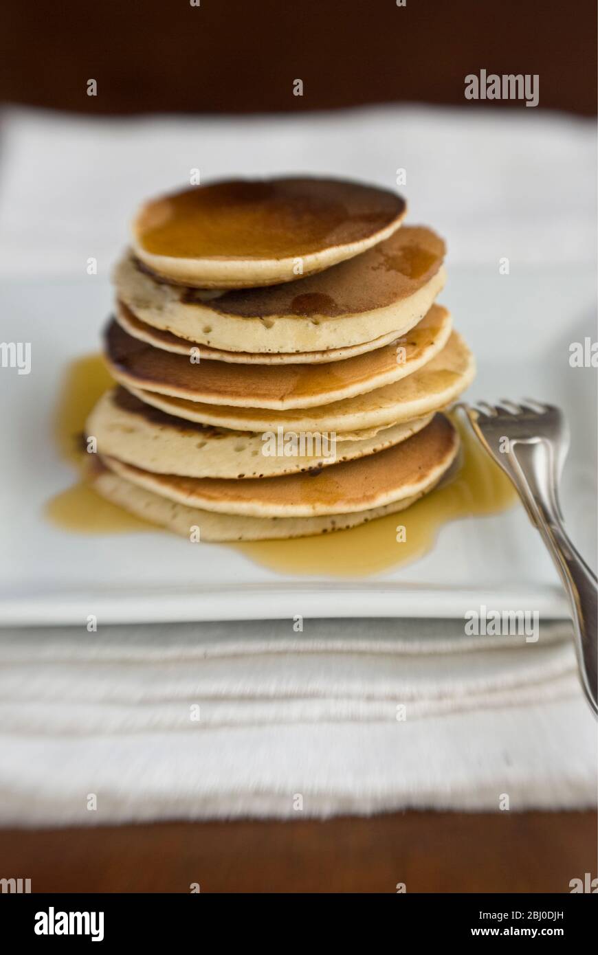 Stapel von schottischen Pfannkuchen auf weißem Teller mit silberner Gabel und Ahornsirup - Stockfoto