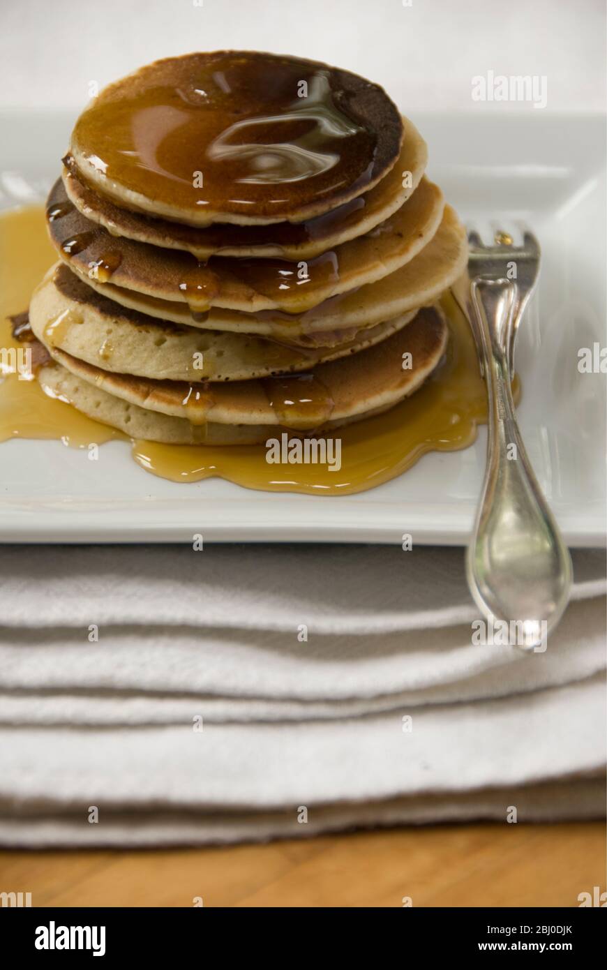 Stapel von schottischen Pfannkuchen auf weißem Teller mit silberner Gabel und Ahornsirup - Stockfoto