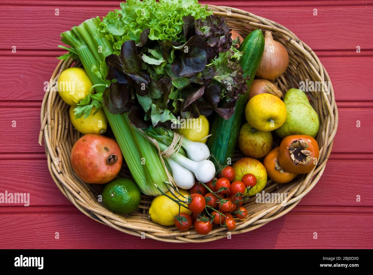Korb mit frischem Obst und Gemüse auf roter Oberfläche - Stockfoto