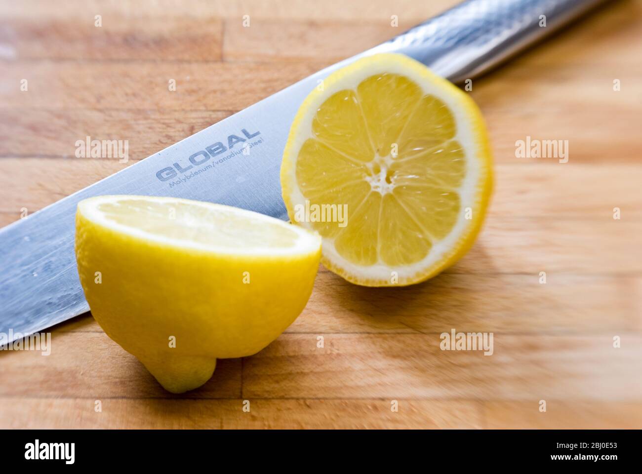Halbierte Zitrone auf Holzbrett, mit Global Messer - Stockfoto