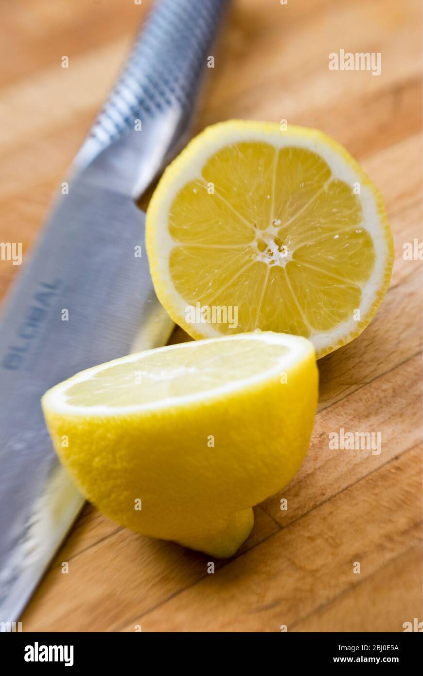 Halbierte Zitrone auf Holzbrett, mit Global Messer - Stockfoto