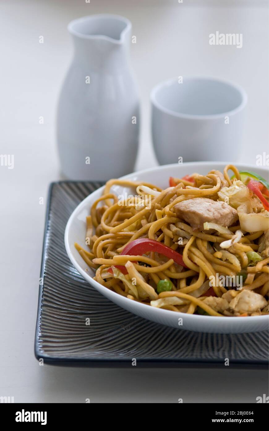 Gebratene Ramen-Nudeln mit Hühnerstücken, Paprika, Bohnensprossen, Zwiebeln und Karotten und mit Sosu, Salz und Pfeffer gewürzt. - Stockfoto