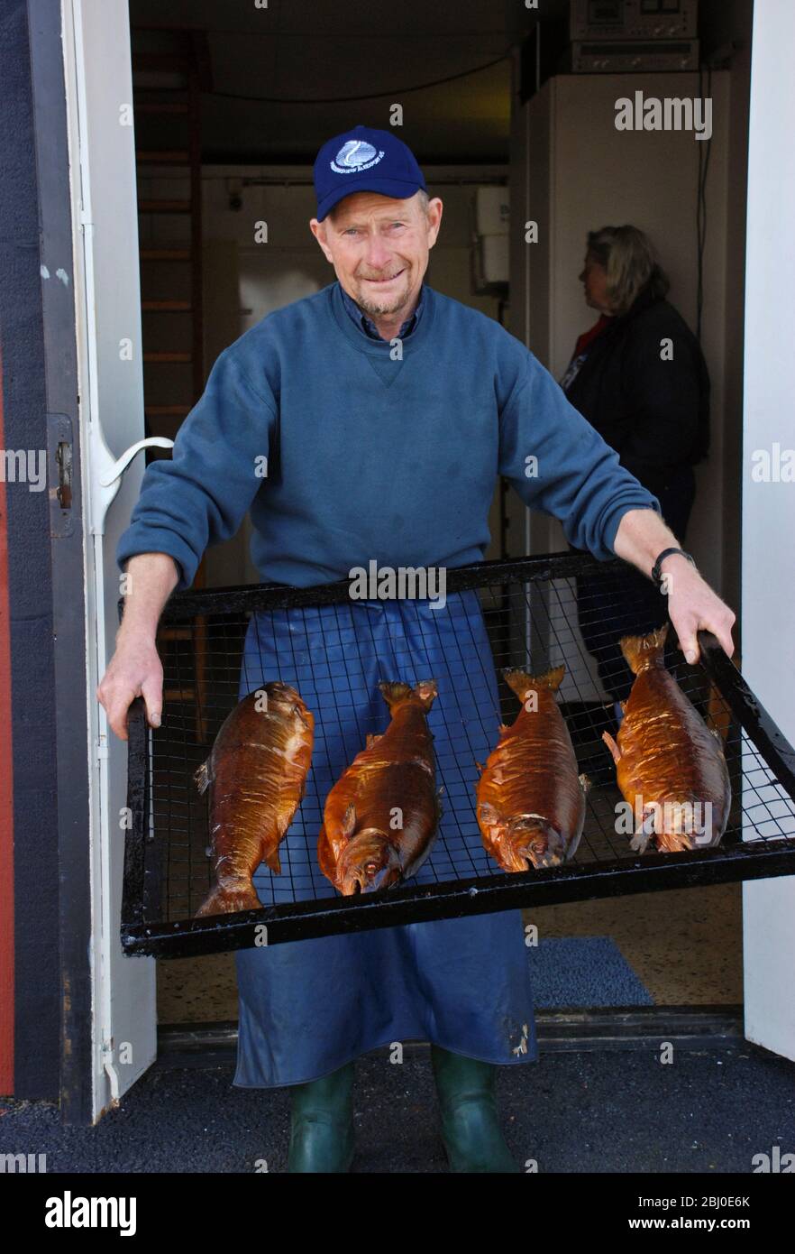 Mann hält Tablett mit frisch geräuchertem Lachs in der Fischräucherei in Donsa, Schweden. Norwegischer Fjordlachs wird kalt geräuchert über Erlenholz-Chips achtern Stockfoto