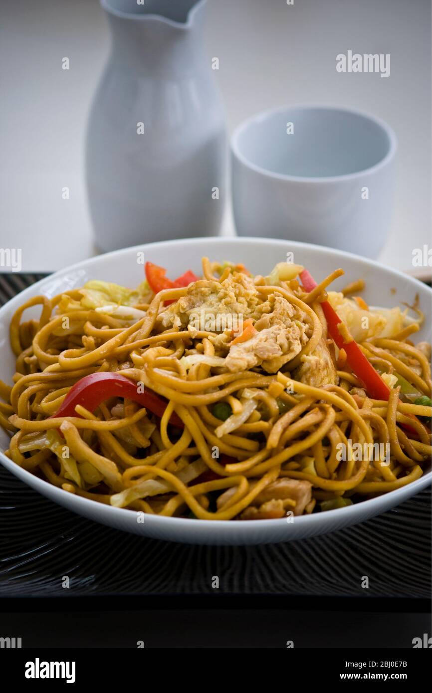 Gebratene Ramen-Nudeln mit Hühnerstücken, Paprika, Bohnensprossen, Zwiebeln und Karotten und mit Sosu, Salz und Pfeffer gewürzt. - Stockfoto