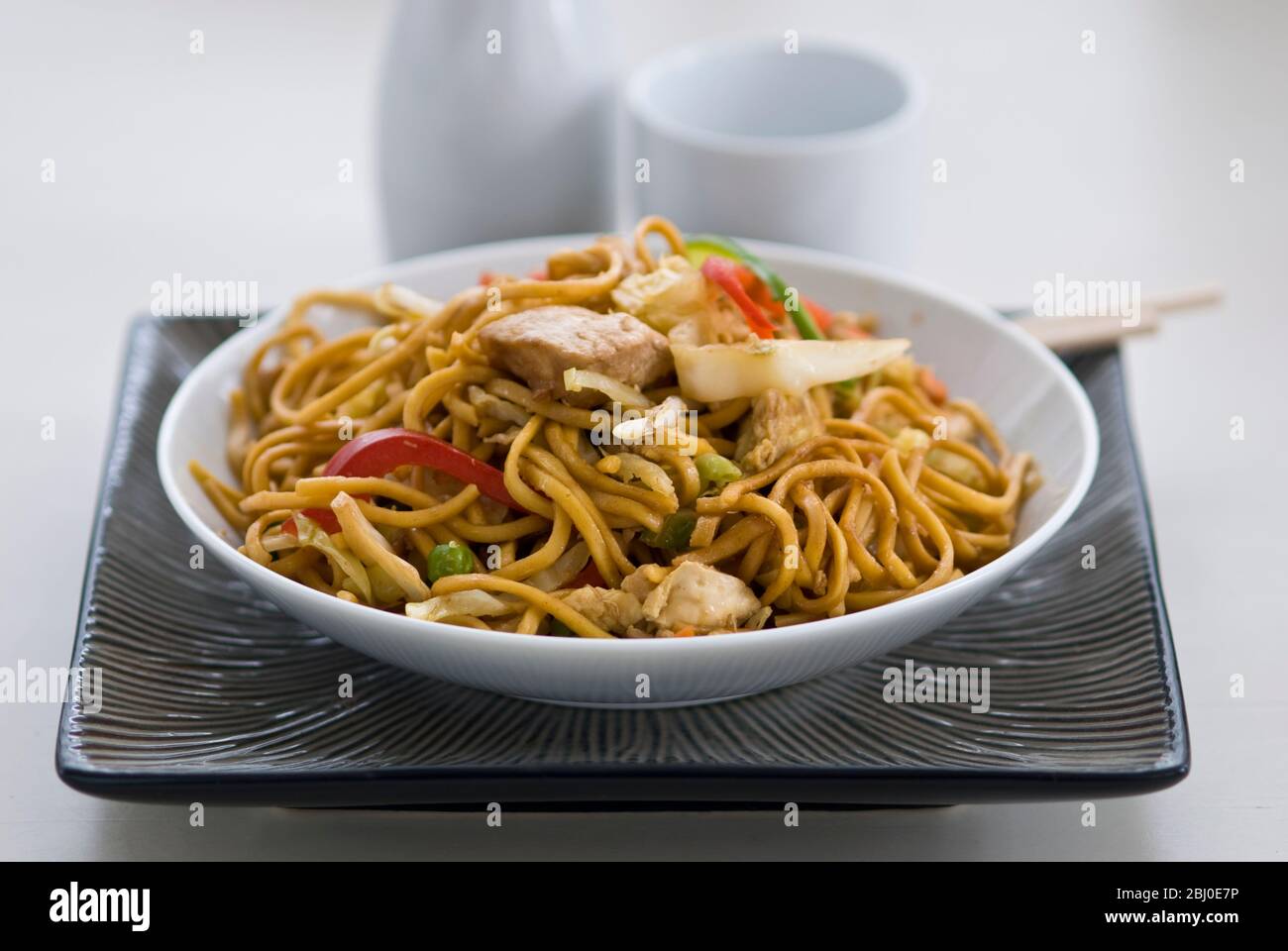 Gebratene Ramen-Nudeln mit Hühnerstücken, Paprika, Bohnensprossen, Zwiebeln und Karotten und mit Sosu, Salz und Pfeffer gewürzt. - Stockfoto