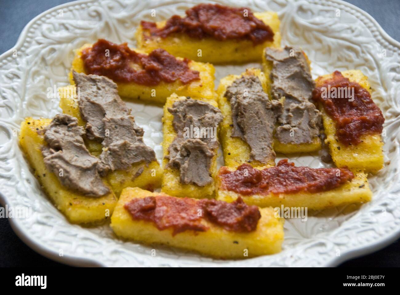 Teller von Crostini aus Polenta in Olivenöl frittiert mit Hühnerleber Pastete oder getrocknete Tomaten Verbreitung, serviert mit Getränken - Stockfoto