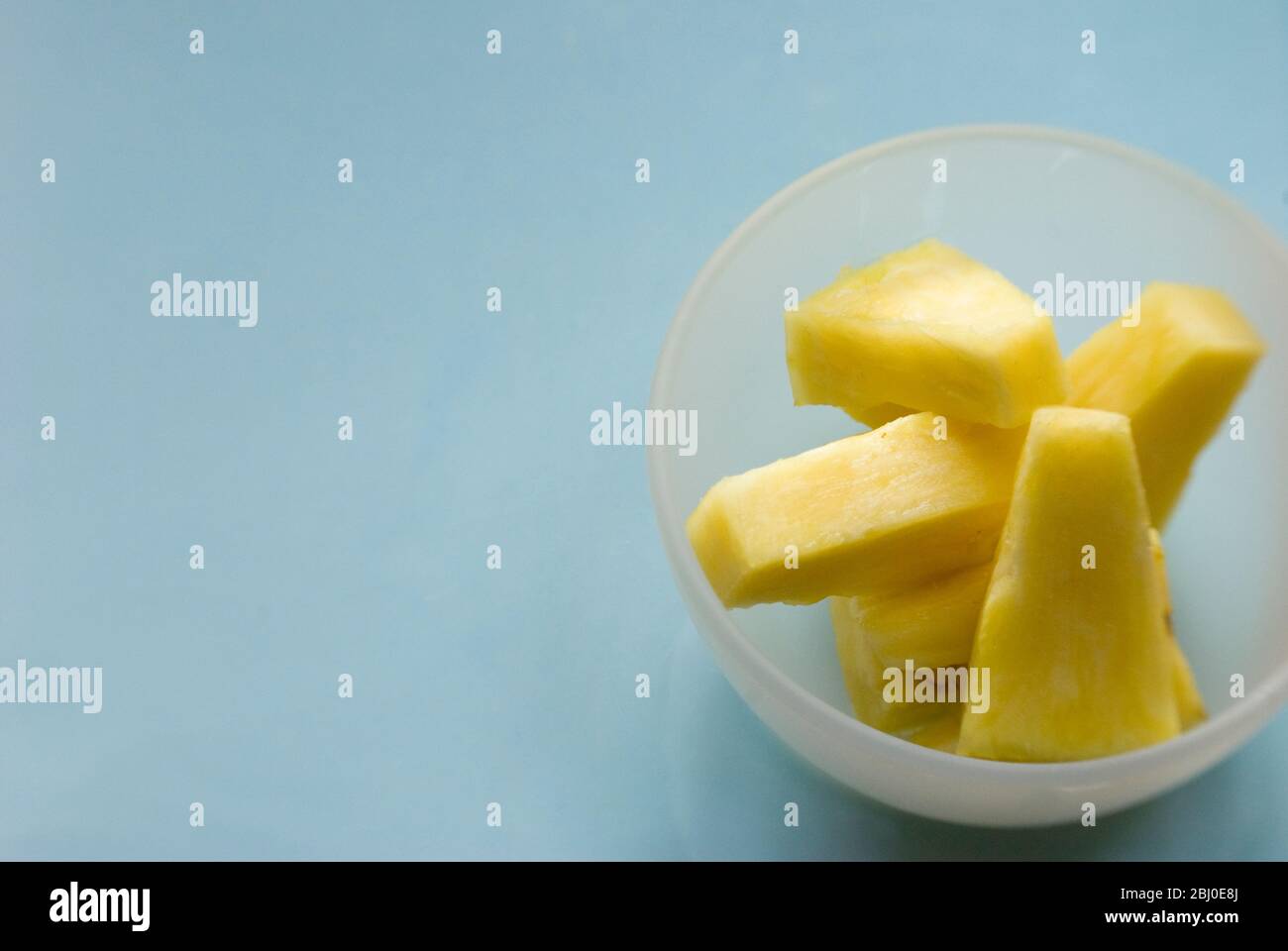 Stücke von frischer Ananas, die aus der ganzen Frucht in einer kleinen Glasschüssel geschnitten werden - Stockfoto