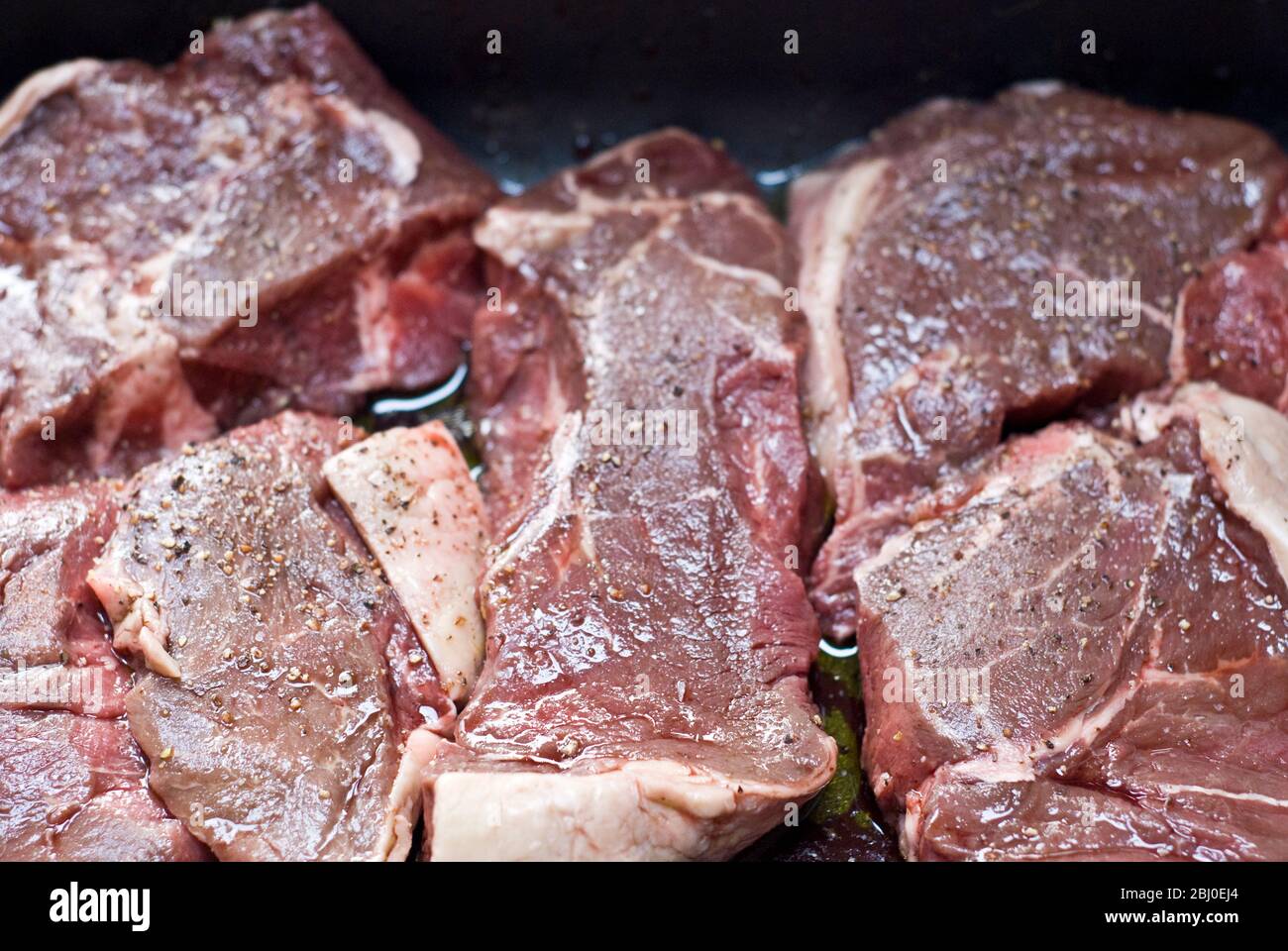 Stücke von Rumpsteak, die in Olivenöl, Rotwein und schwarzem Pfeffer mariniert werden - Stockfoto