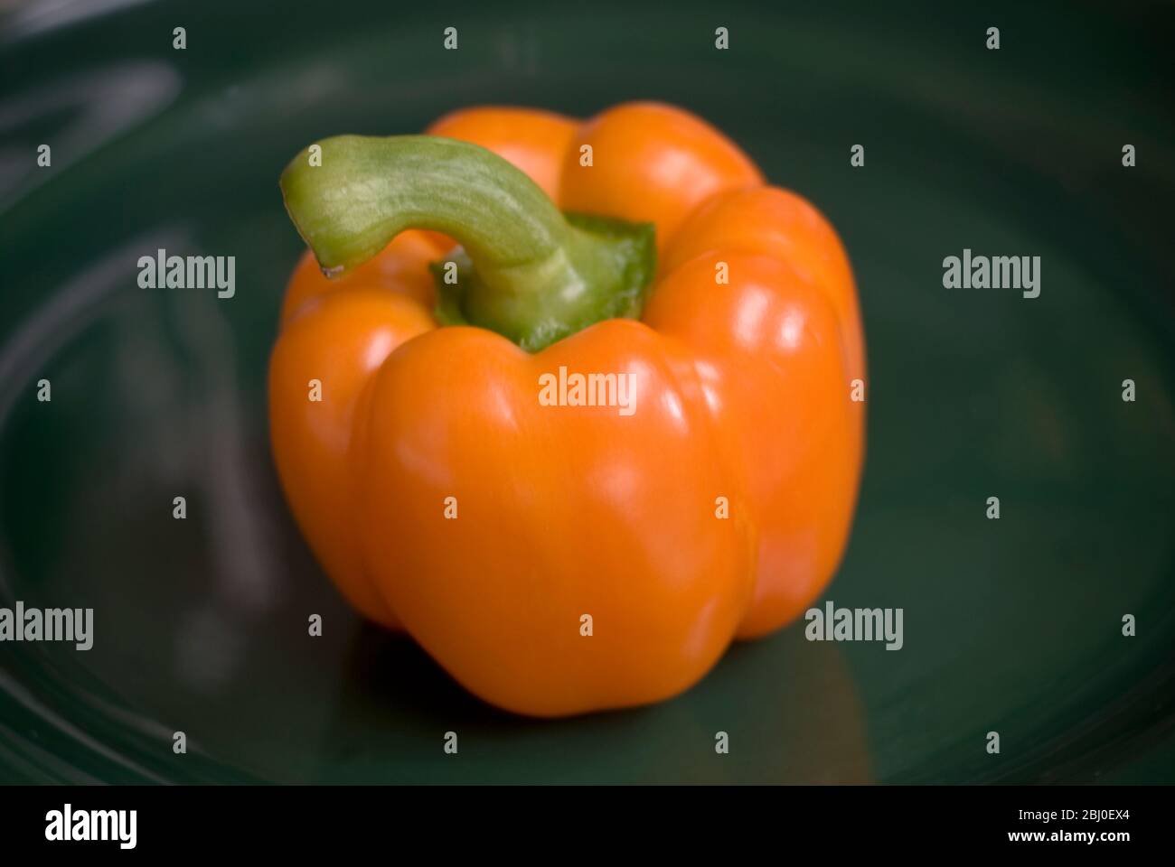 Orangenpfeffer auf dunkelgrüner Platte - Stockfoto
