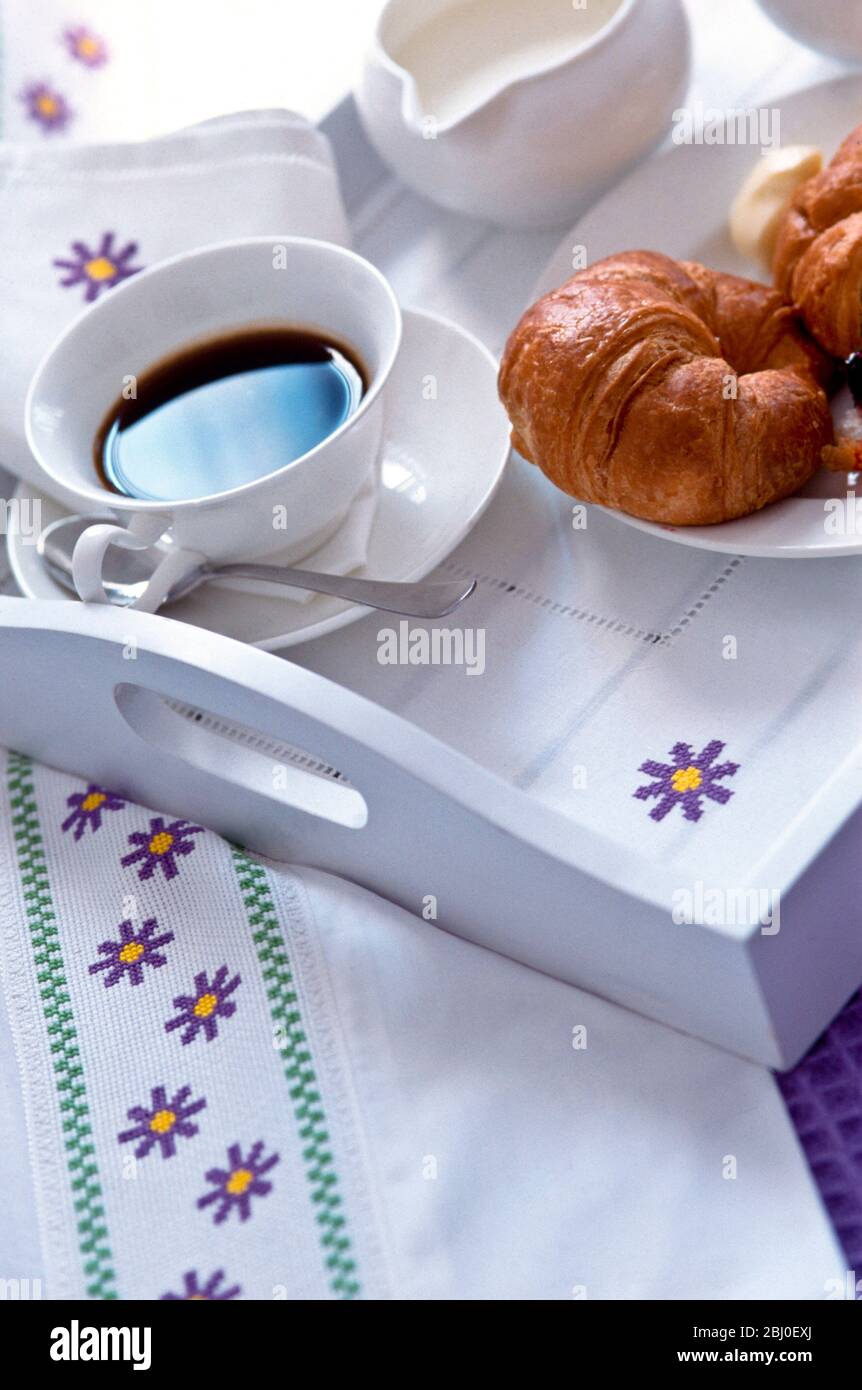 Frühstück mit schwarzem Kaffee und Croissants auf bemaltem Tablett mit handbesticktem Traycloth ausgekleidet - Stockfoto
