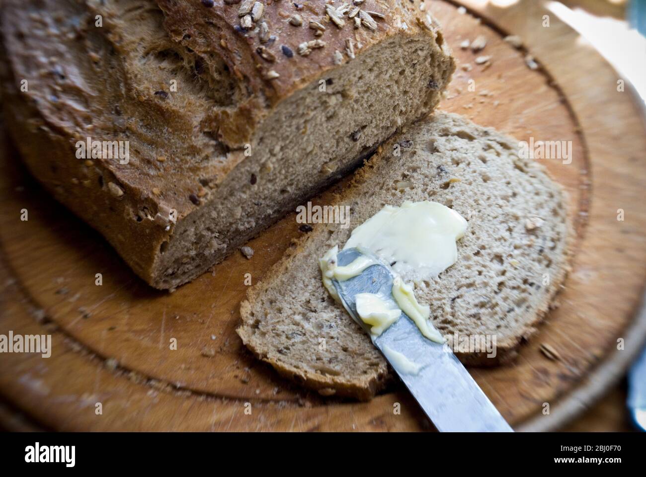 Eine Scheibe Brot aus Vollkorn, Roggen und Walnussbrot auf einem alten Holzbrett zu butteren. - Stockfoto