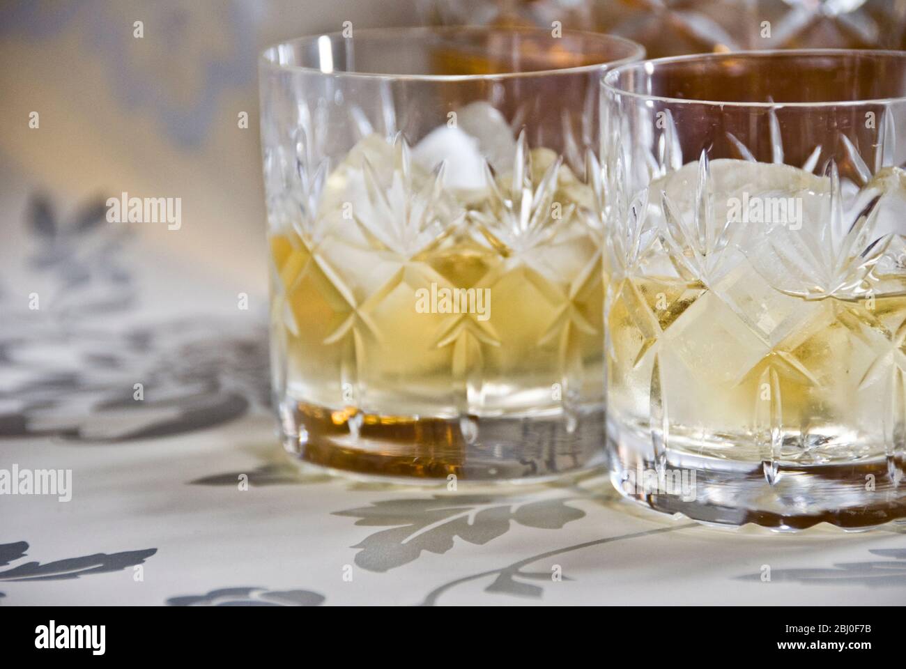 Scotch Whisky auf Eis in geschliffenem Bleikristall auf dekorativer Silberoberfläche, mit Dekanter. - Stockfoto