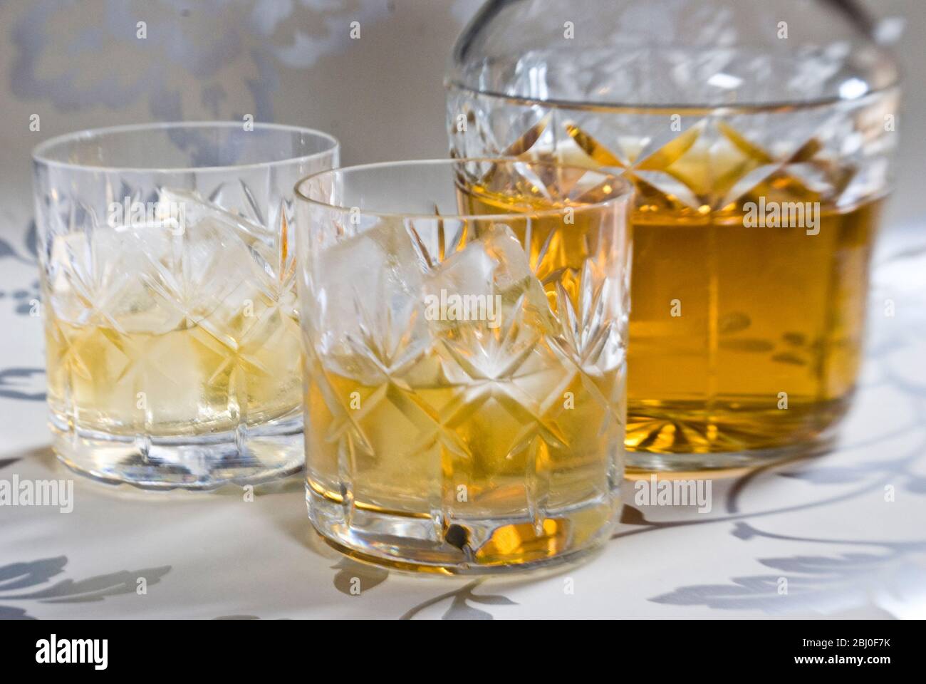 Scotch Whisky auf Eis in geschliffenem Bleikristall auf dekorativer Silberoberfläche, mit Dekanter. - Stockfoto