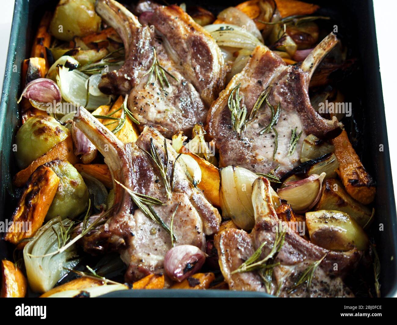 Schweinebraten mit gemischtem Bratgemüse, gewürzt mit schwarzem Pfeffer und frischen Rosmarinzweigen. - Stockfoto