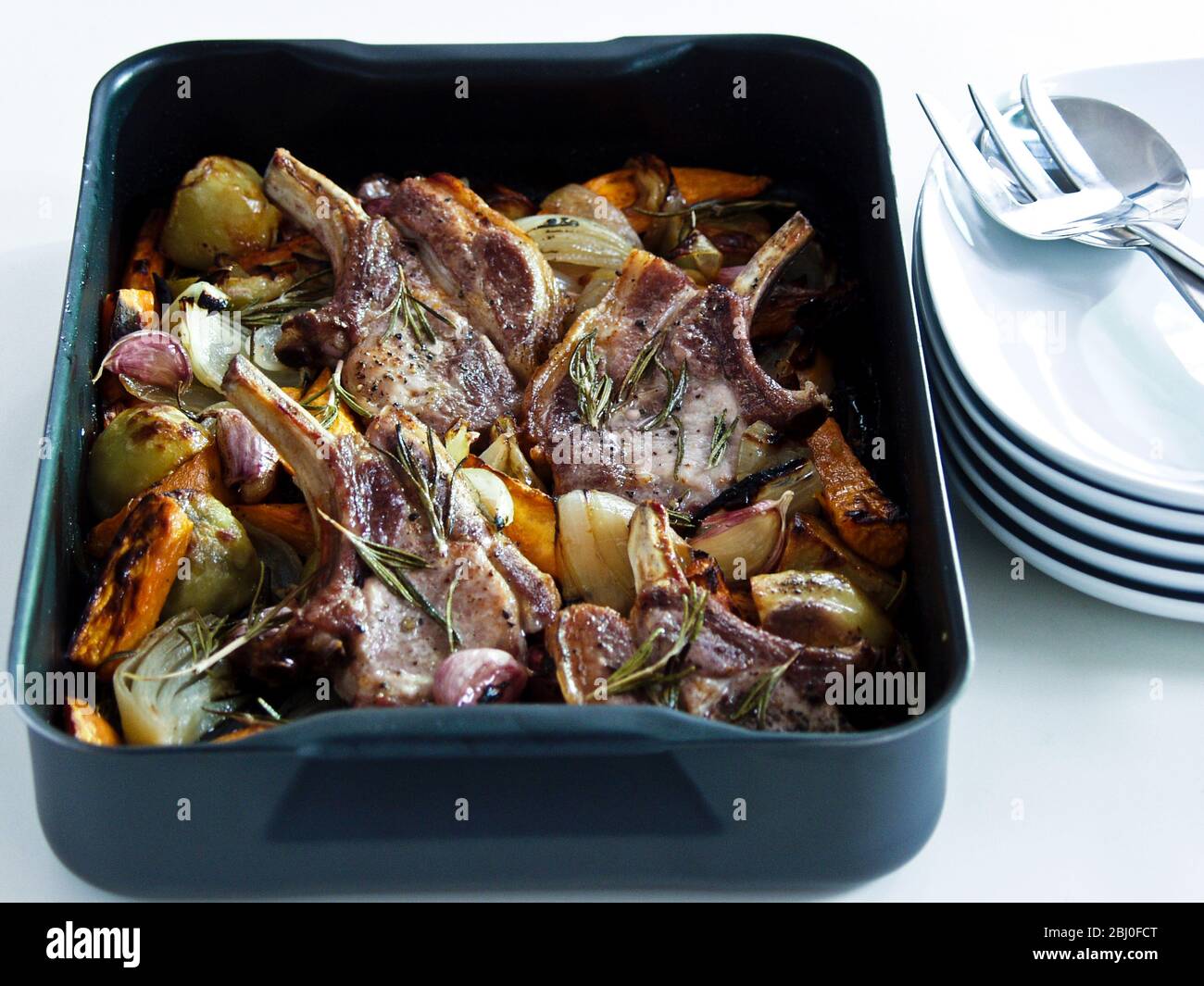 Schweinebraten mit gemischtem Bratgemüse, gewürzt mit schwarzem Pfeffer und frischen Rosmarinzweigen. - Stockfoto