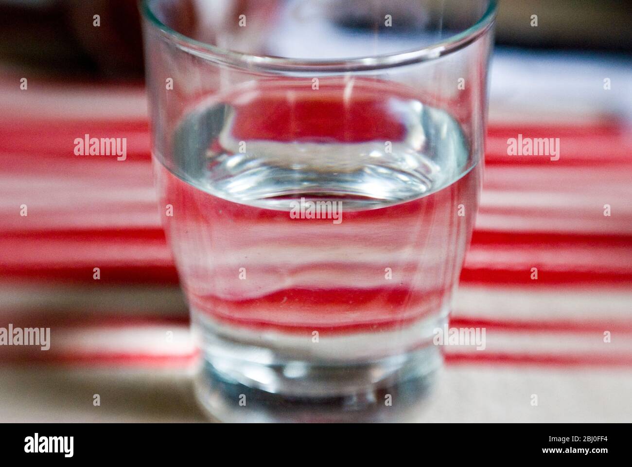 Glas Wasser auf rot-cremefarbenem gestreiftem Tuch. Aufgenommen mit einer Lensbaby-Linse für unscharfe Kanten - Stockfoto