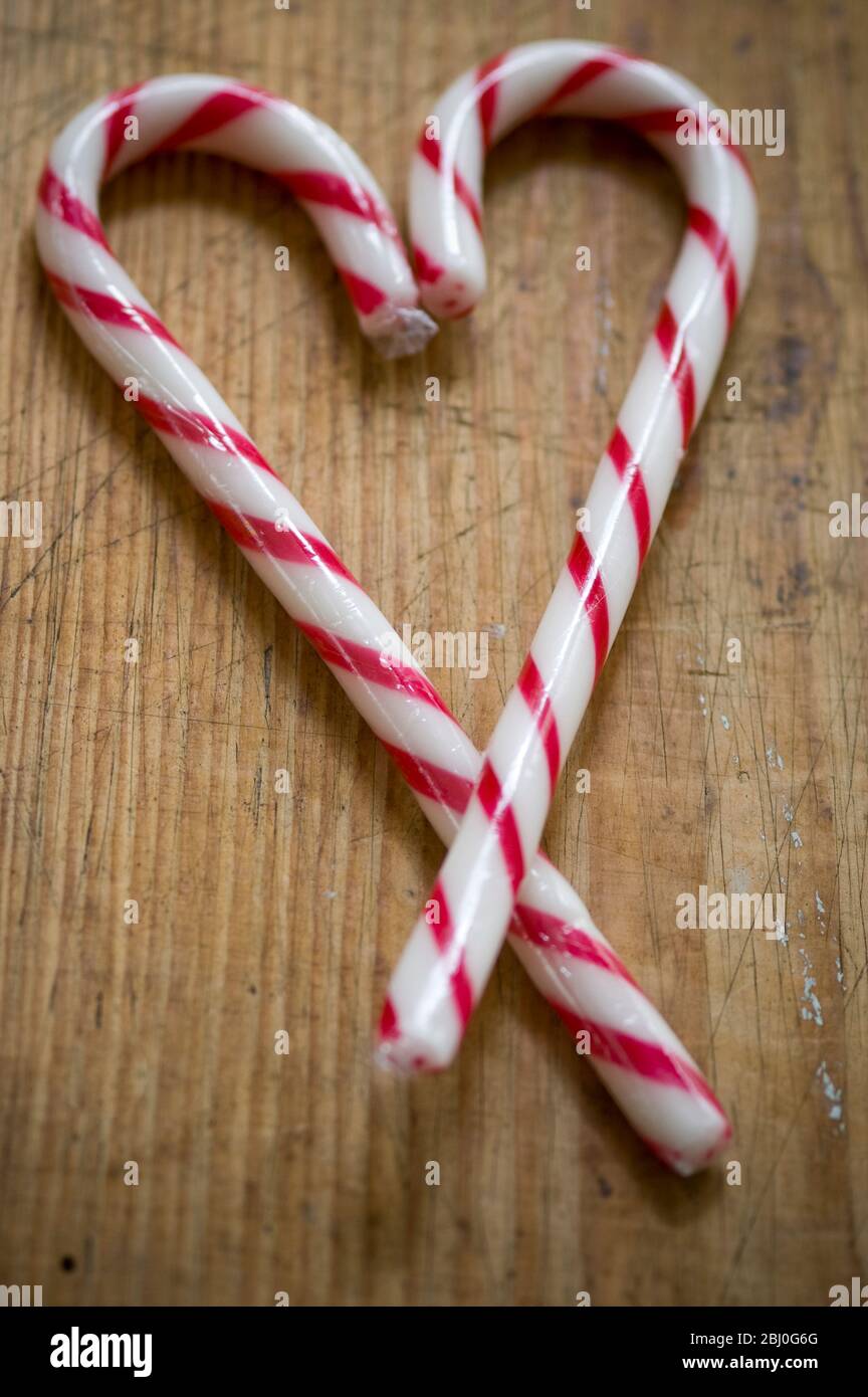 Zwei rot-weiß gestreifte Bonbonstöcke auf Holzfläche gekreuzt, um Herzform zu machen. - Stockfoto