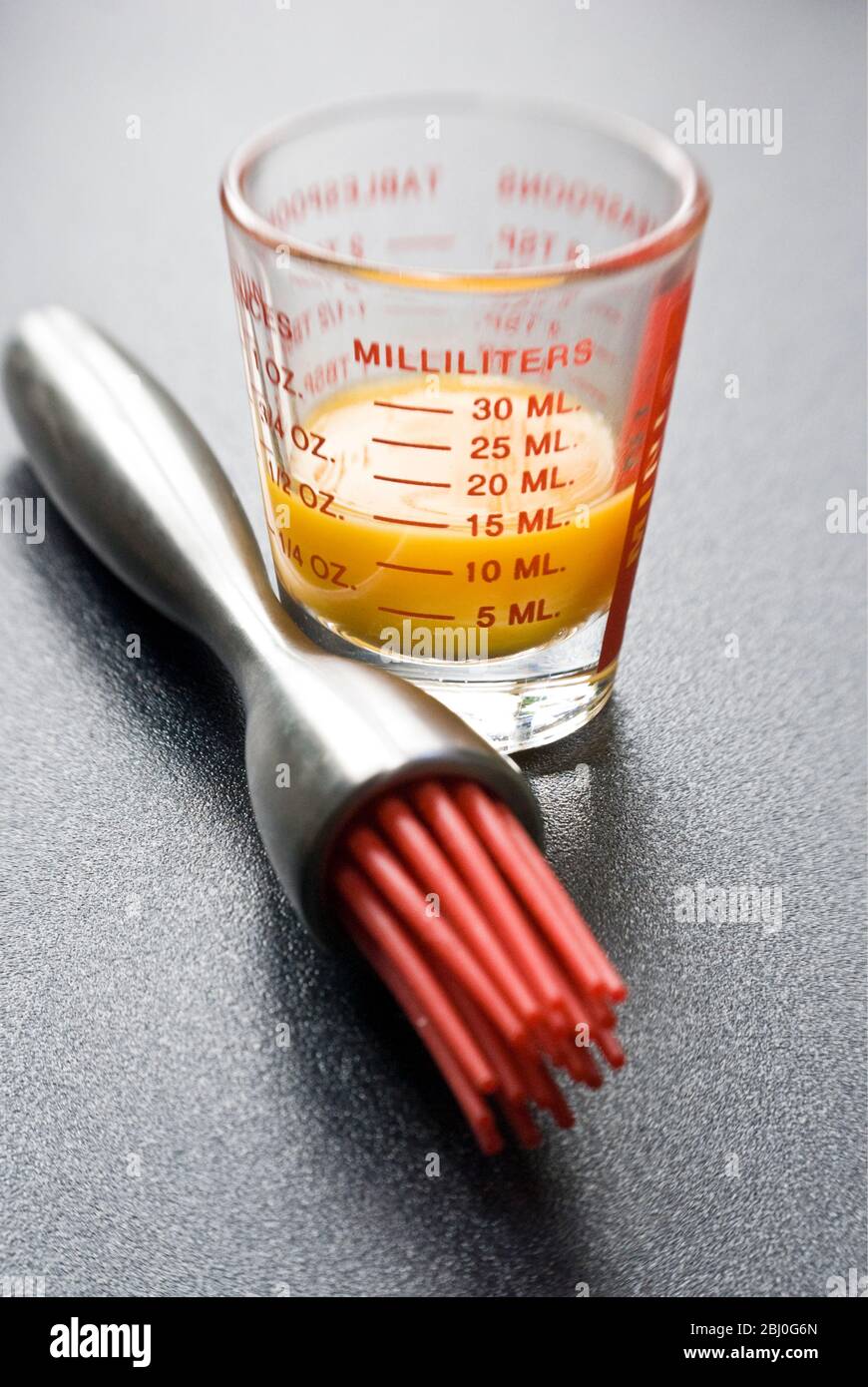 Eigelb in kleinem Glas Messglas mit moderner Teigbürste mit roten Silikon-Borsten - Stockfoto