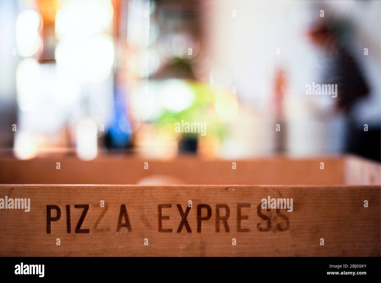 Das Innere des Pizza Express Restaurants zeigt beschriftete hölzerne Lieferbox und verschwommene Figuren und Details im Hintergrund - Stockfoto
