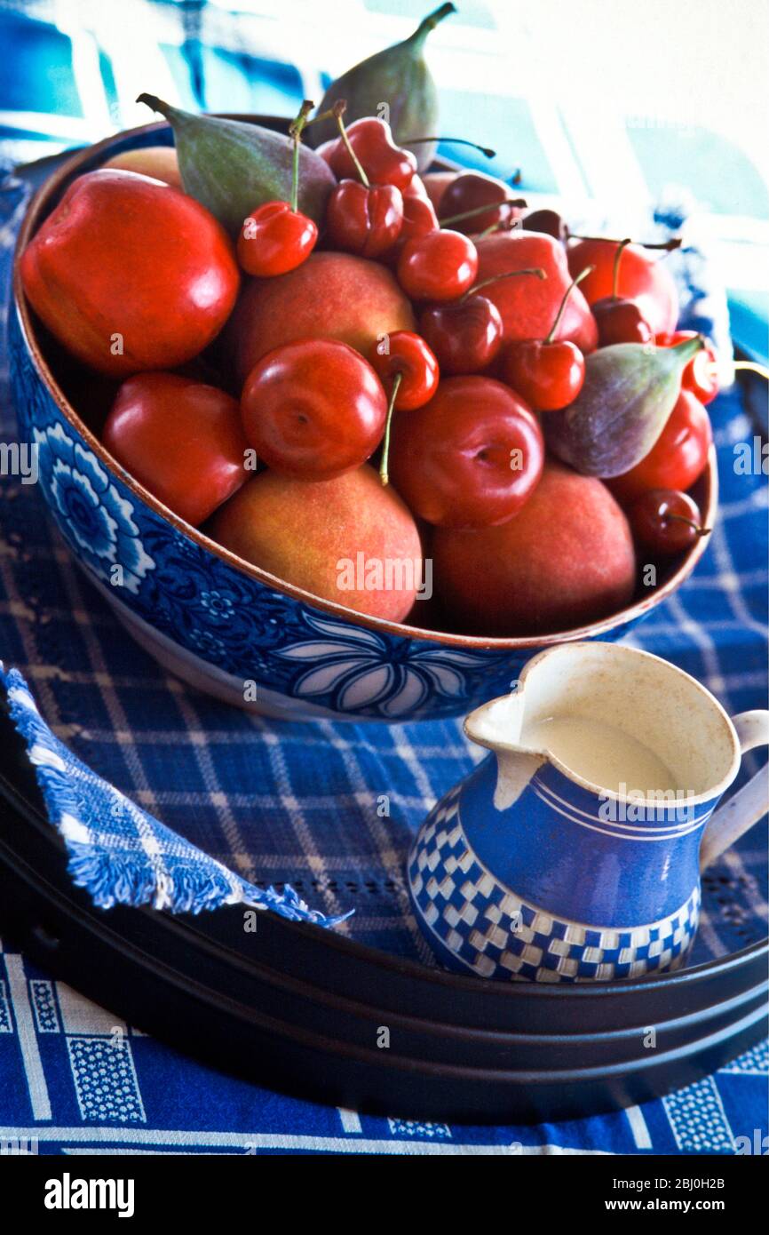 Große Obstschale aus Pflaumen, Kirschen, Pfirsichen. Äpfel und Feigen auf blauem Tuch, auf Tablett. - Stockfoto