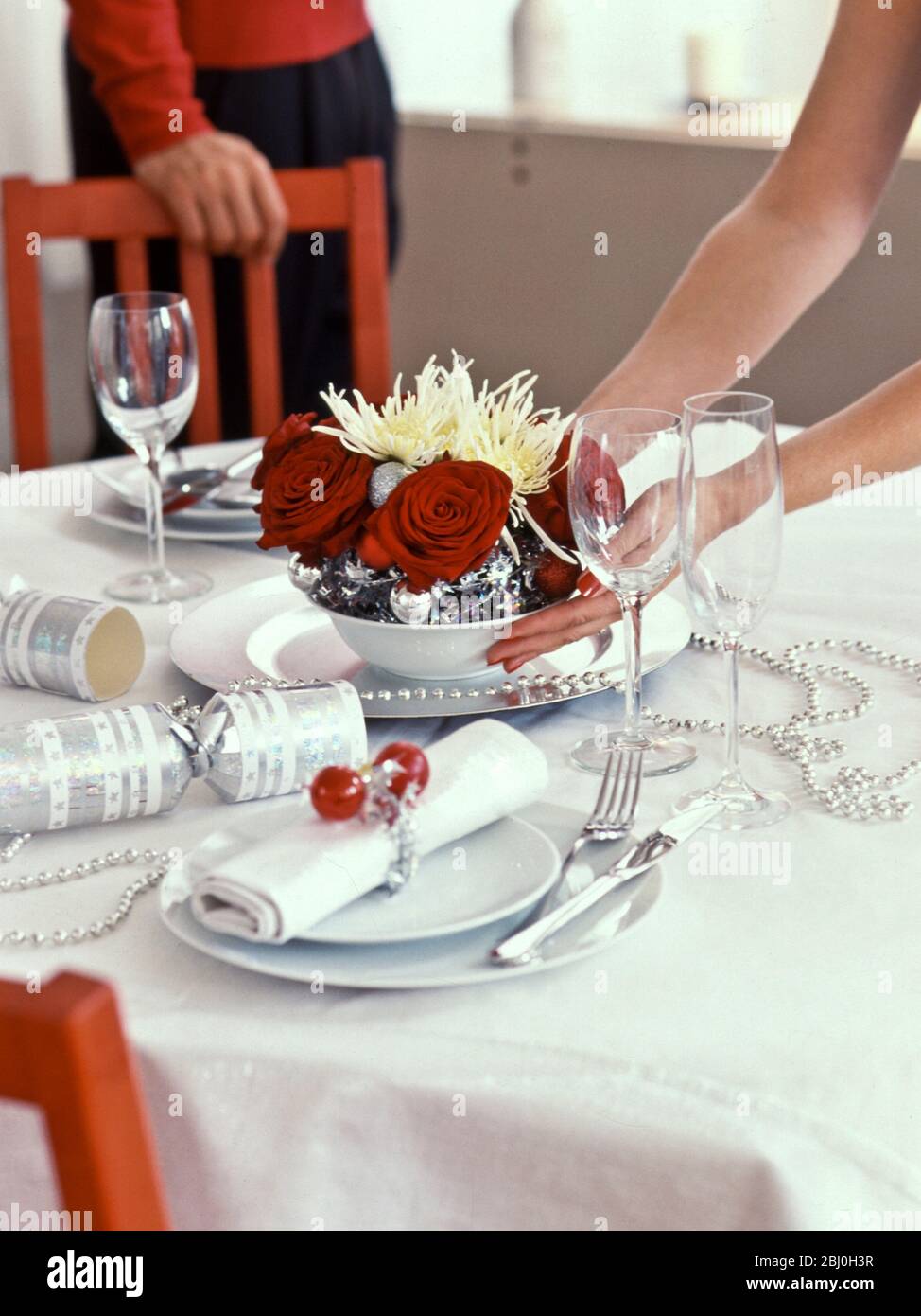 Weihnachtliche Tischdekoration aus tiefroten Rosen und stacheligen Chrysanthemen mit silbernen Kugeln, die auf den Tisch gestellt werden - Stockfoto