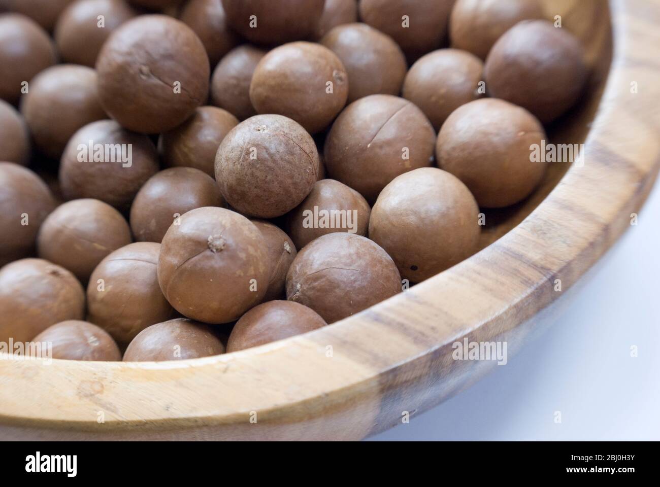 Ganze Macadamianüsse in ihren Schalen in Holzschale - Stockfoto
