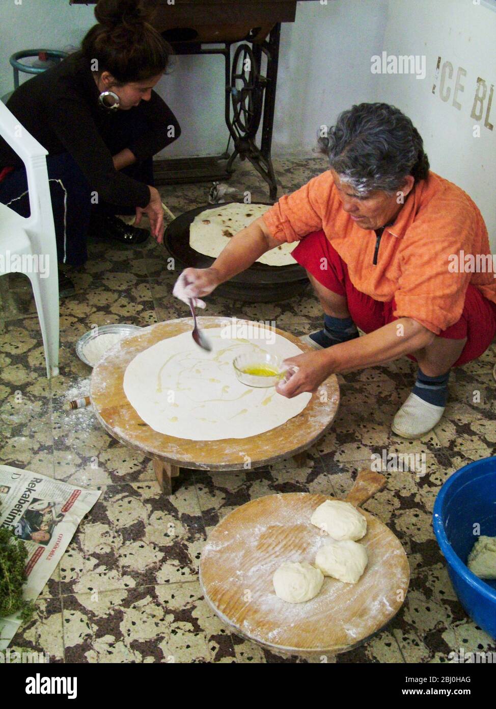 Türkische Frau Bäcker Rollen große dünne Kreise von Brot auf einem runden Holzbrett auf dem Boden der Kai Bäckerei. Hinter ihr steht die gasgefeuerte Heizplatte Stockfoto