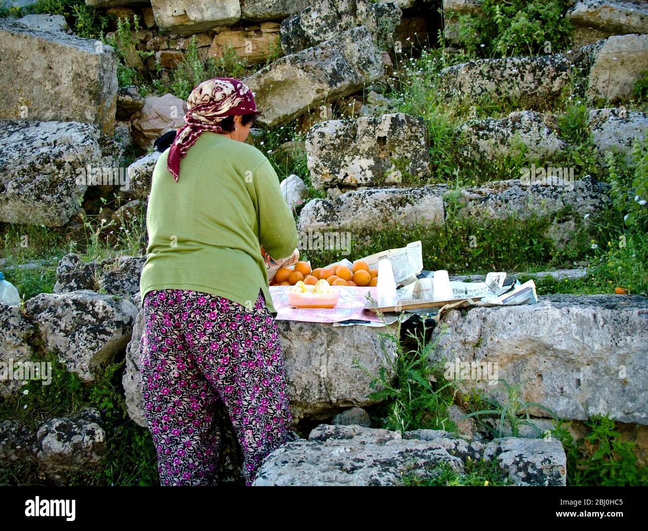 Frau quetscht Orangen, um Gläser mit frischem Saft an Touristen im antiken griechischen Amphitheater im Süden der Türkei zu verkaufen - Stockfoto